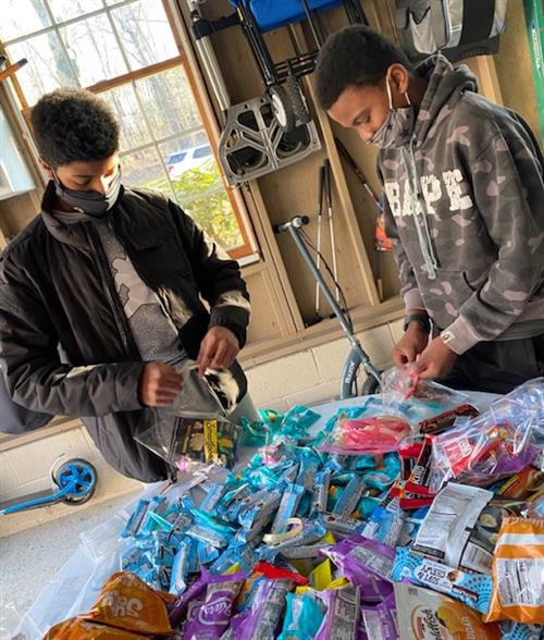 Two boys stand at a table putting snacks in cellophane bags. 